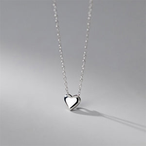 Two heart-shaped pendant necklaces, one with a gold plating and the other in silver, displayed against a grey background.