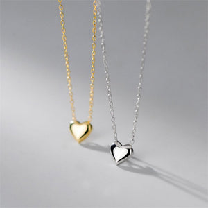Two heart-shaped pendants on gold and silver chains against a gray background