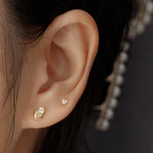 Close-up of an ear wearing gold heart-shaped earrings with a blurred background