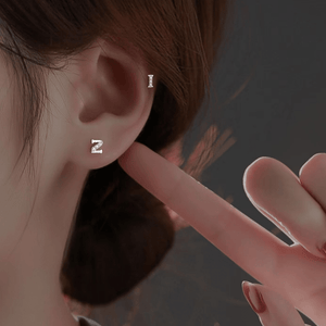 Close-up of an ear wearing a silver earring with a hand pointing towards it against a dark background