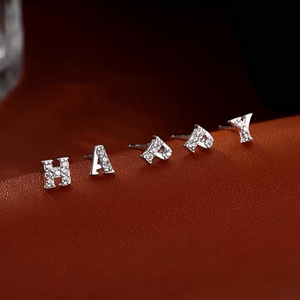 Silver letter earrings spelling 'HAPPY' on a brown surface