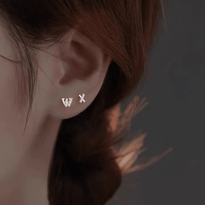 Close-up of an ear wearing 'W' and 'X' earrings with a blurred background
