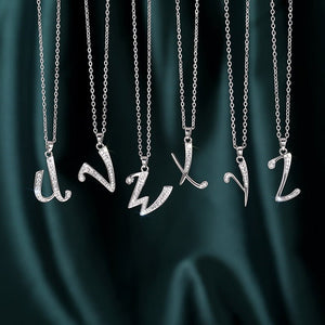 Silver necklaces with letter pendants on a dark green fabric background