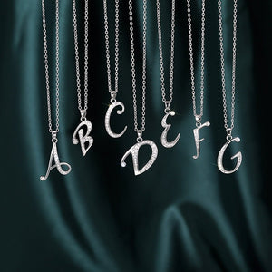 Silver necklaces with letter pendants on a dark green fabric background