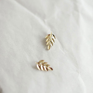 Gold leaf-shaped earrings on a light fabric background