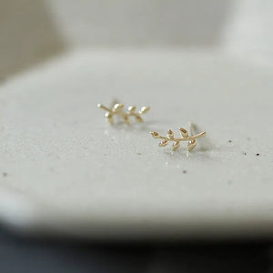 Gold leaf-shaped earrings on a light gray surface