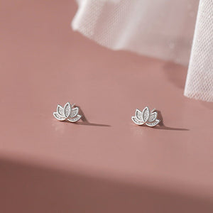 A set of two lotus flower stud earrings, one plated in silver and the other in gold, displayed against a pink background.