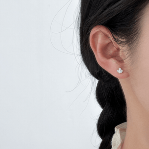 Close-up of an ear wearing a silver leaf-shaped earring on a light gray background