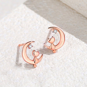A pair of stud earrings featuring a crescent moon with a cat silhouette, displayed in both silver and rose gold finishes.