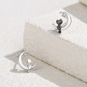 A pair of stud earrings featuring a crescent moon with a cat silhouette, displayed in both silver and rose gold finishes.