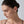Close-up of a woman wearing a diamond earring against a neutral background