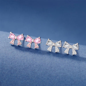 Two set of bow tie stud earrings in pink and silver colors, made with sterling silver and cubic zirconia, displayed against a blue background.