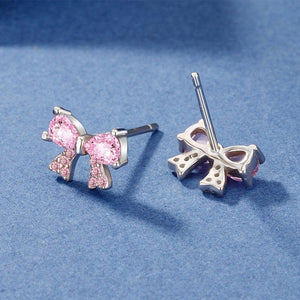 Pair of silver bow-shaped earrings with pink cubic zirconia on a blue background