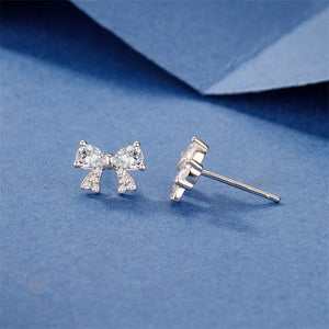 Pair of silver bow-shaped earrings with colorless cubic zirconia on a blue background