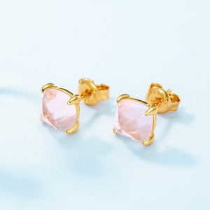 A pair of small pink rose quartz stud earrings with gold plating on a white background.