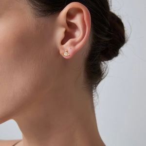 Close-up of an ear wearing a gold earring with a clear gemstone on a neutral background