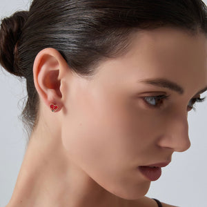 Close-up of a woman wearing red heart-shaped earrings against a neutral background
