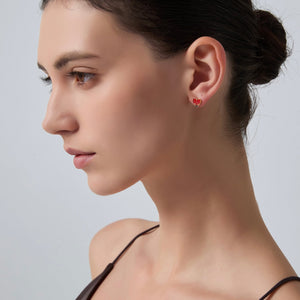 Close-up of a woman wearing red heart-shaped earrings against a neutral background