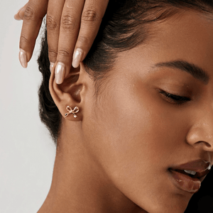 Close-up of a woman wearing a gold bow-shaped earring on a neutral background