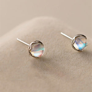 A pair of round moonstone stud earrings with gold plating, displayed on a beige surface.
