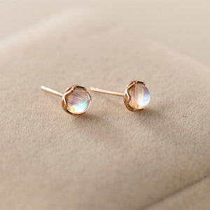 A pair of round moonstone stud earrings with gold plating, displayed on a beige surface.