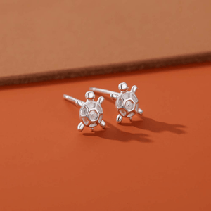 Silver sea turtle earrings on an orange background