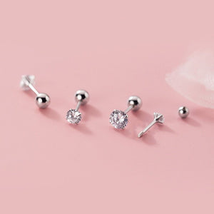 Set of silver stud earrings with clear gemstones on a pink background