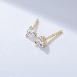 Gold earrings with clear gemstones on a light gray background