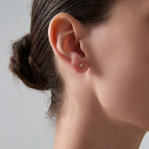 Close-up of an ear wearing a gold star-shaped earring against a neutral background