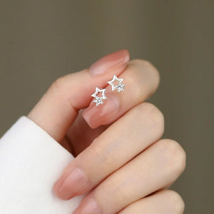 Star-shaped earrings held between fingers against a neutral background
