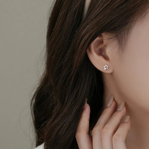 Star-shaped earring worn by a person with dark hair and beige nail polish.