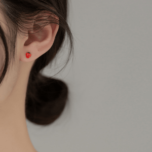 Close-up of an ear wearing a strawberry-shaped earring against a neutral background