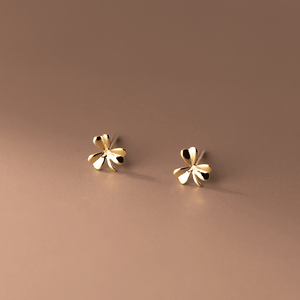 Pair of gold four-leaf clover earrings on a brown background