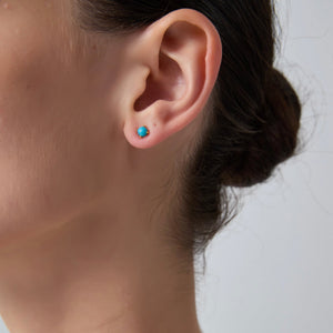 Close-up of an ear wearing a turquoise stud earring with a blurred background