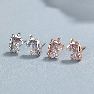 Four pairs of unicorn-shaped earrings in silver and rose gold on a light gray background
