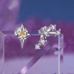 A pair of delicate zodiac stud earrings with one featuring a green cubic zirconia at the center and the other with a white gold plating and smaller white stones.