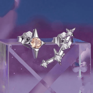 A pair of delicate zodiac stud earrings with one featuring a green cubic zirconia at the center and the other with a white gold plating and smaller white stones.