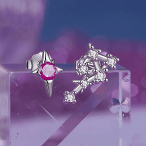 A pair of delicate zodiac stud earrings with one featuring a green cubic zirconia at the center and the other with a white gold plating and smaller white stones.