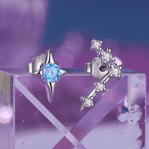 A pair of delicate zodiac stud earrings with one featuring a green cubic zirconia at the center and the other with a white gold plating and smaller white stones.