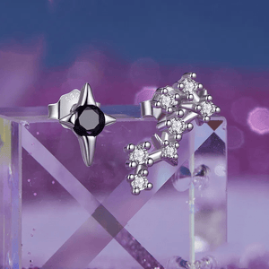 A pair of delicate zodiac stud earrings with one featuring a green cubic zirconia at the center and the other with a white gold plating and smaller white stones.