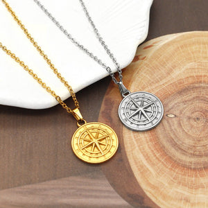 Two compass necklaces, one gold and one silver, on a wooden surface.
