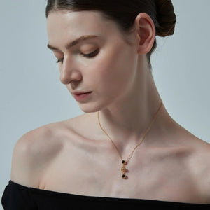 Woman wearing a gold necklace with black stones on a plain background
