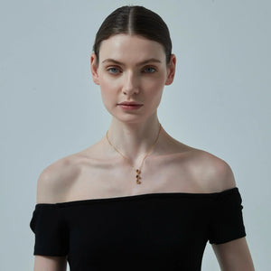 Woman wearing a black off-shoulder top and gold necklace against a light gray background