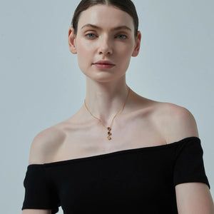 Woman wearing a black off-shoulder top and gold necklace against a light gray background