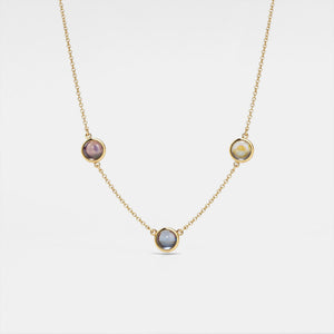 Gold necklace with three round gemstones on a light gray background