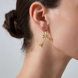 Gold bow-shaped earring worn by a person with a neutral background