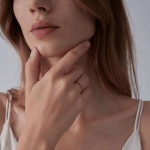 Woman wearing a gold ring with a blue evil eye charm on a white background