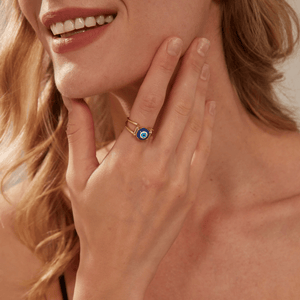 Woman wearing a gold ring with a blue evil eye design on a white background