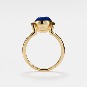 A gold-colored statement cocktail ring with a blue enamel evil eye design on a white background.
