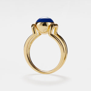 A gold-colored statement cocktail ring with a blue enamel evil eye design on a white background.